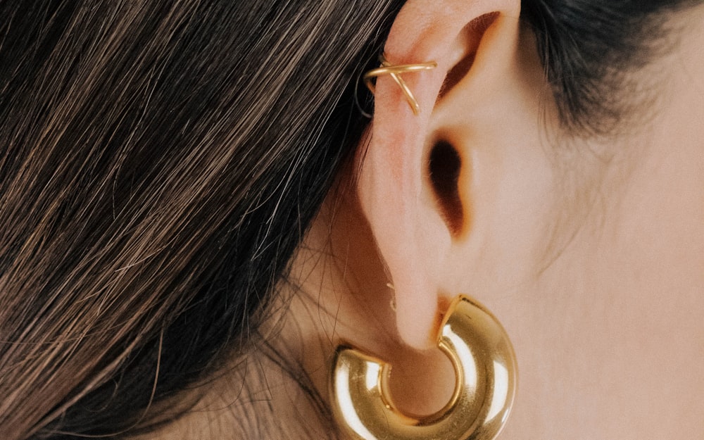 Ear cuff doré fin croisé sur l'hélix, porté avec une créole dorée épaisse au lobe.