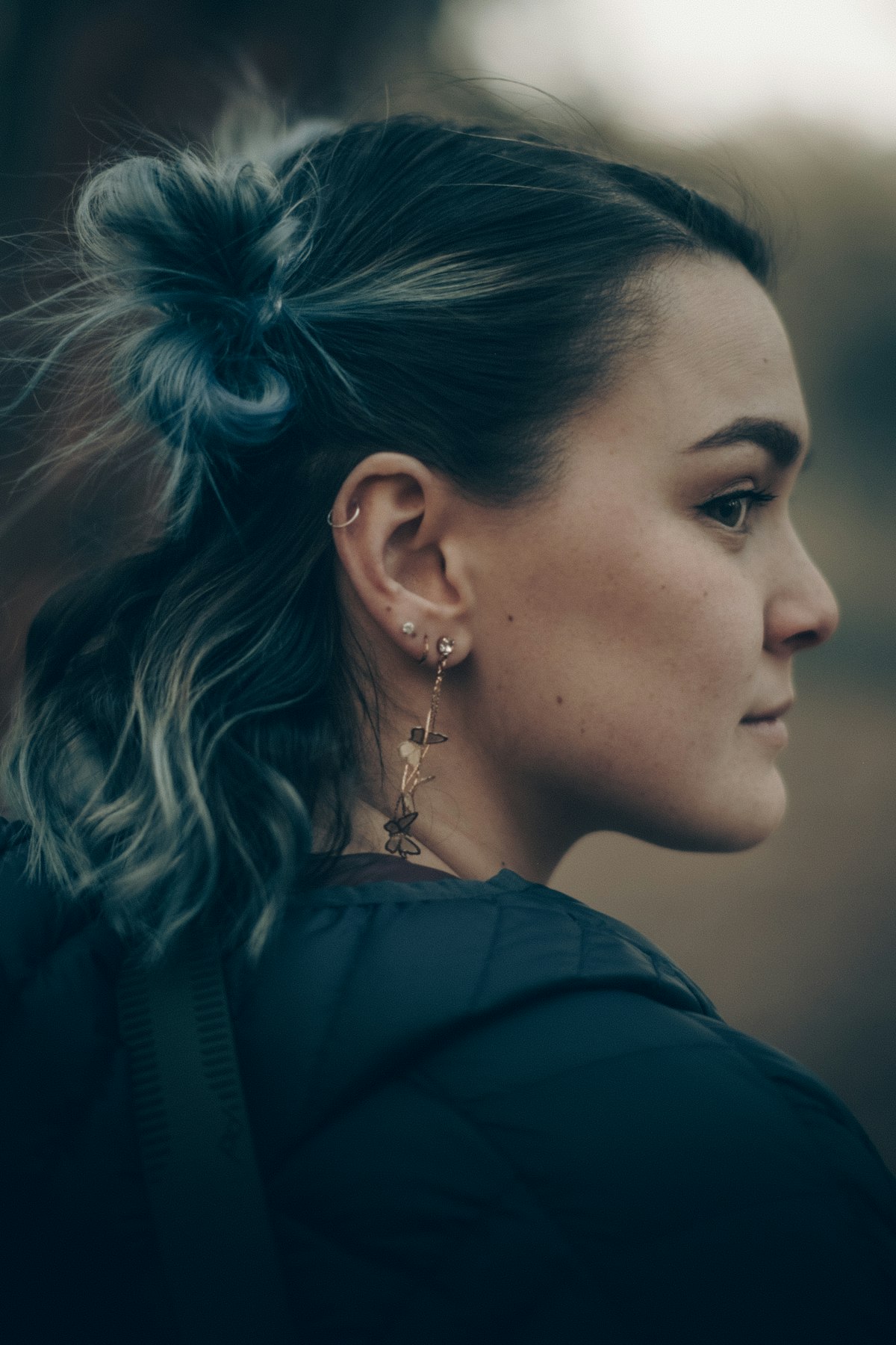 Oreille de profil portant un anneau d'hélix, deux puces au lobe et une longue boucle pendante assortie.