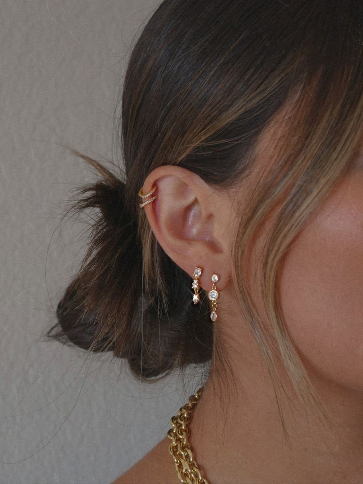 Woman's ear with a gold ear cuff and delicate gemstone earrings.