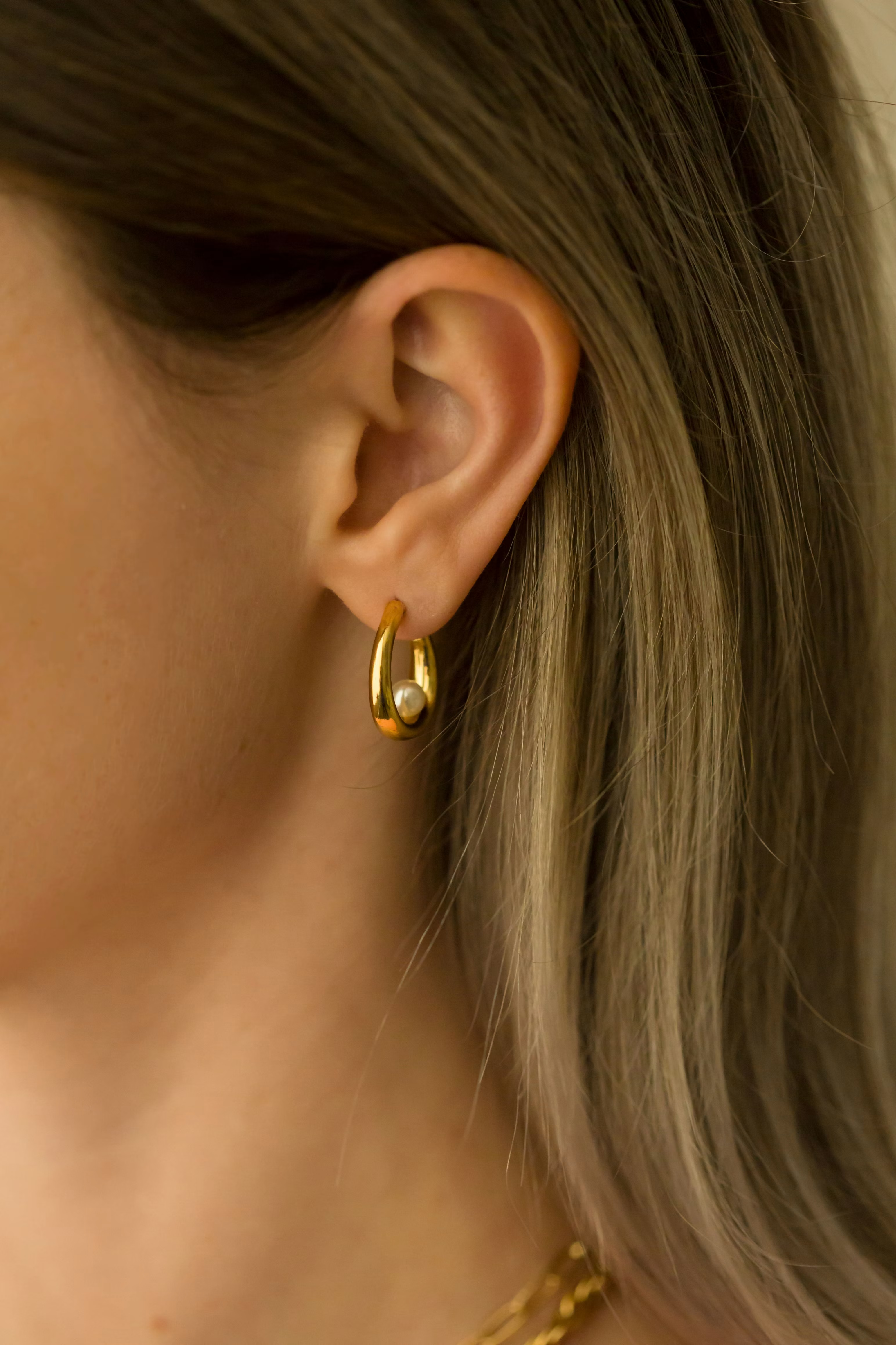 Boucles d'oreilles minimalistes dorées posées sur une surface claire, esthétique épurée.