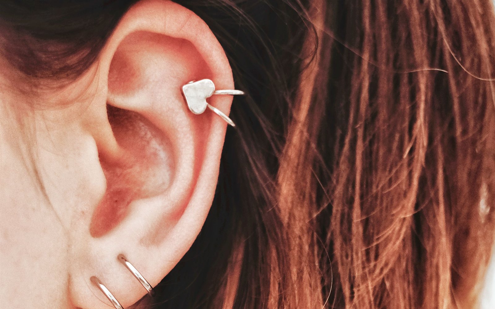 Gros plan d'une oreille féminine portant un bijou d'hélix en forme de cœur et deux anneaux de lobe.