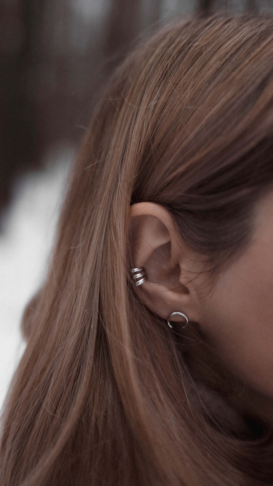 Ear adorned with delicate titanium and gold piercings, suitable for sensitive skin.