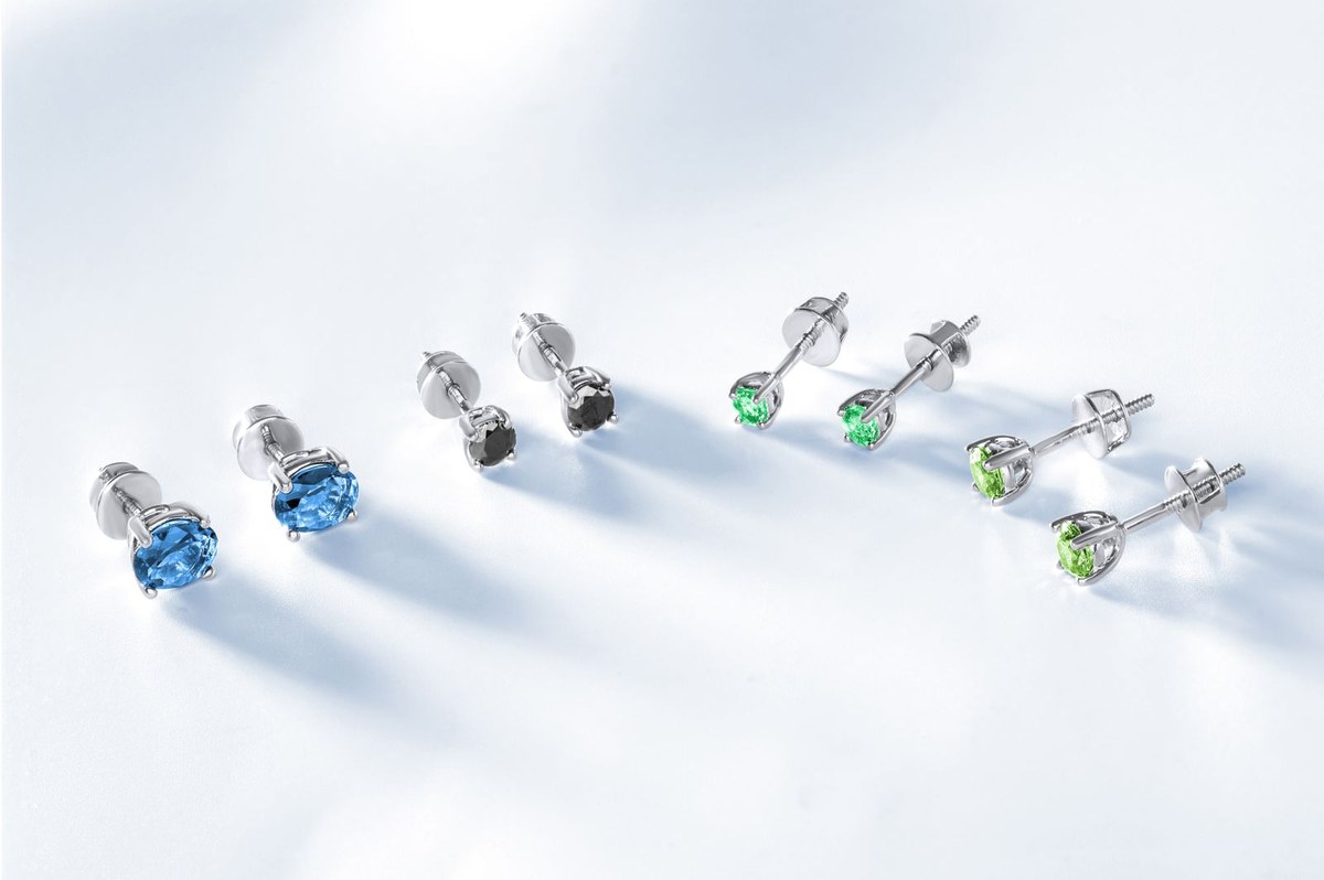 Puces d'oreille serties de pierres bleues, noires et vertes, tiges filetées visibles sur fond clair