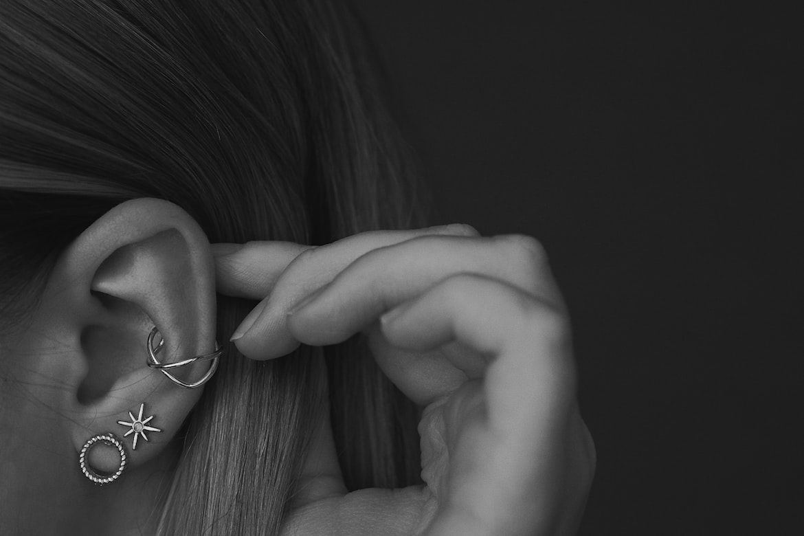 Woman's ear with several piercings, ear cuff and studs, in a curated ear style.